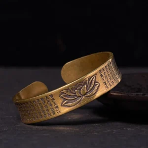 Heart Sutra lotus open cuff bracelet in polished brass, showing detailed lotus flower engraving and sutra inscriptions on dark surface