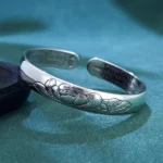 Heart Sutra Lotus copper open adjustable bracelet bangle with embossed lotus and leaf patterns, inner engraved Buddhist scripture, left oblique top-down view on dark teal velvet backdrop