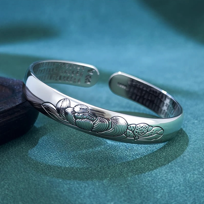 Heart Sutra Lotus copper open adjustable bracelet bangle with embossed lotus and leaf patterns, inner engraved Buddhist scripture, left oblique top-down view on dark teal velvet backdrop