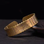 Heart Sutra lotus open cuff bracelet with engraved Buddhist sutra and delicate lotus flower design in antiqued brass finish, shown on dark display surface
