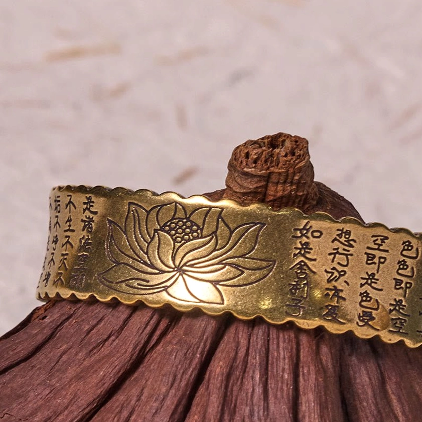 Heart Sutra lotus engraved open cuff bracelet with scalloped edges displayed on wooden incense holder, bronze tone finish