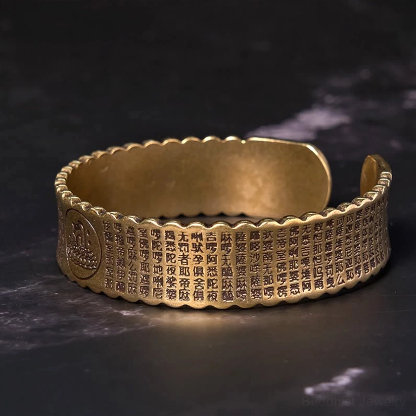 Side angle view of Heart Sutra lotus cuff bracelet with full sutra engravings covering the open bangle design in vintage bronze tone