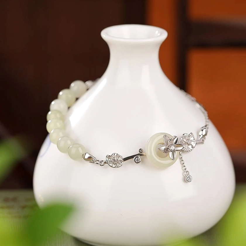 Silver Hetian jade bracelet close-up side view with pale jade beads and silver floral accents wrapped on ceramic vase