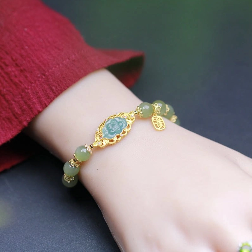 Woman wearing Hetian jade lotus bracelet on wrist with red fabric sleeve, close-up view showing gold-toned hardware and matching jade beads fit
