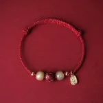 Red braided Buddhist protection bracelet with Hetian jade beads and hand-carved cinnabar lotus pendant, 14K gold plated charm, top-down flat lay view