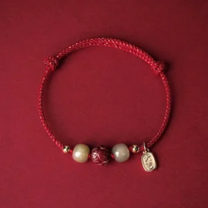 Red braided Buddhist protection bracelet with Hetian jade beads and hand-carved cinnabar lotus pendant, 14K gold plated charm, top-down flat lay view