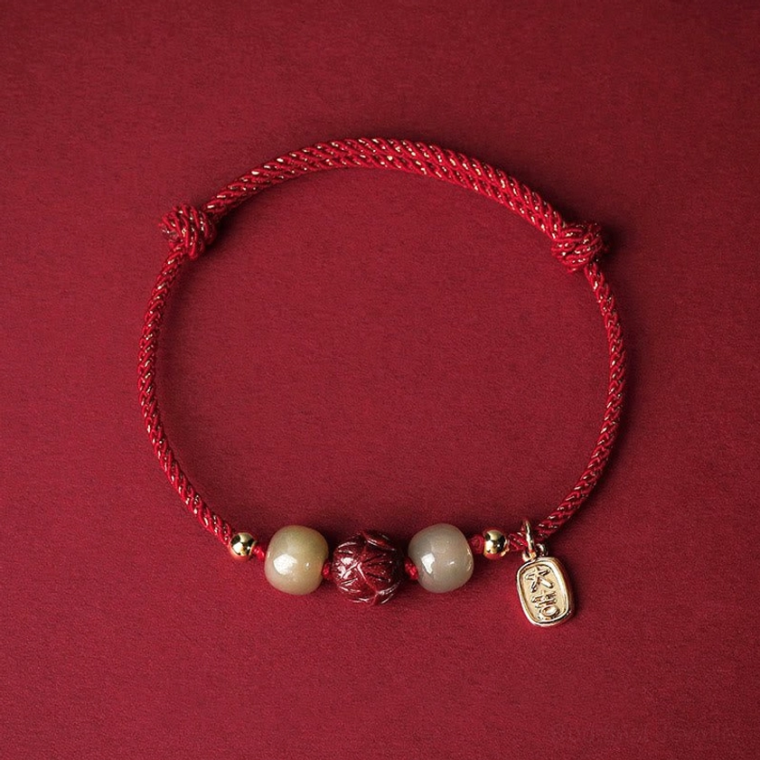 Red braided Buddhist protection bracelet with Hetian jade beads and hand-carved cinnabar lotus pendant, 14K gold plated charm, top-down flat lay view