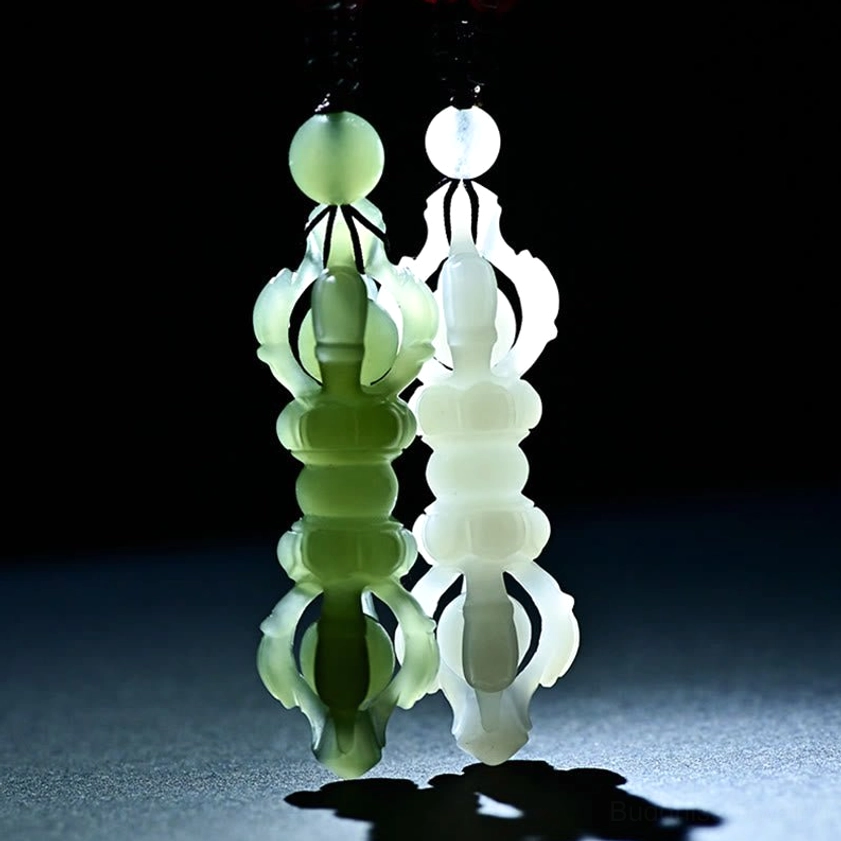Two Hetian jade Dorje Vajra pendants in celadon and white jade, direct front view with spotlight, showing hollow carved Buddhist symbol design