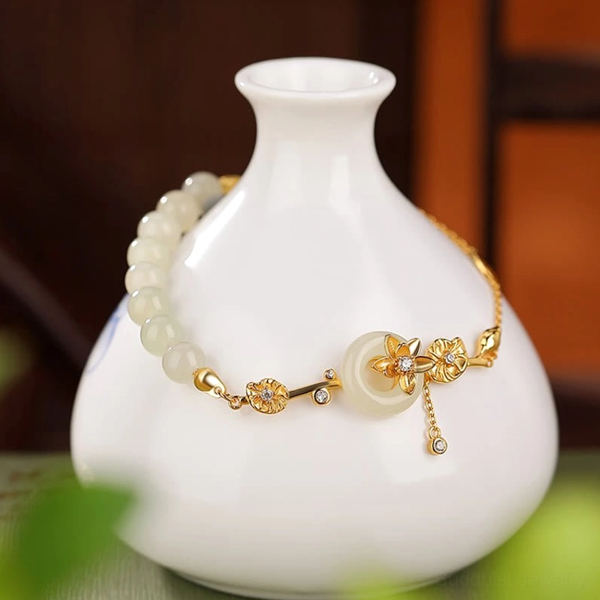 Close-up side view of gold-toned Hetian jade bracelet with lotus flower charm wrapped on white ceramic vase