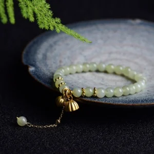 Hetian jade lotus bracelet with gold charms displayed on blue ceramic tray, top-down view with natural styling
