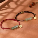 Hetian jade lotus prosperity bracelet with red woven cord and gold charm displayed on warm fabric with dried botanical elements, showcasing the handcrafted adjustable design