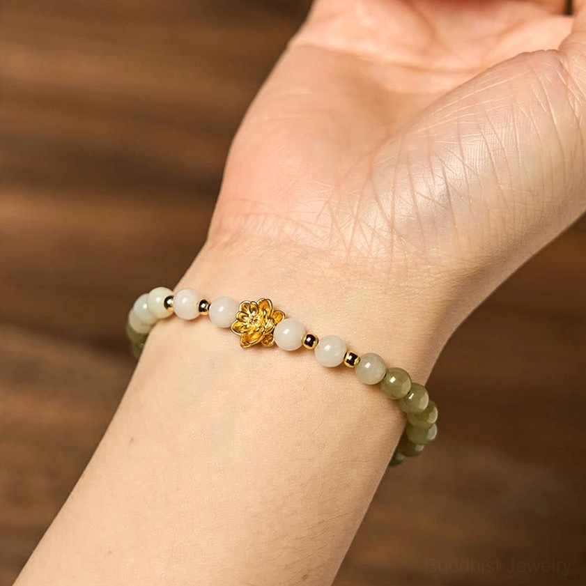 Delicate jade lotus bracelet worn on wrist against wooden table, showing refined gradient effect and gleaming gold lotus accent