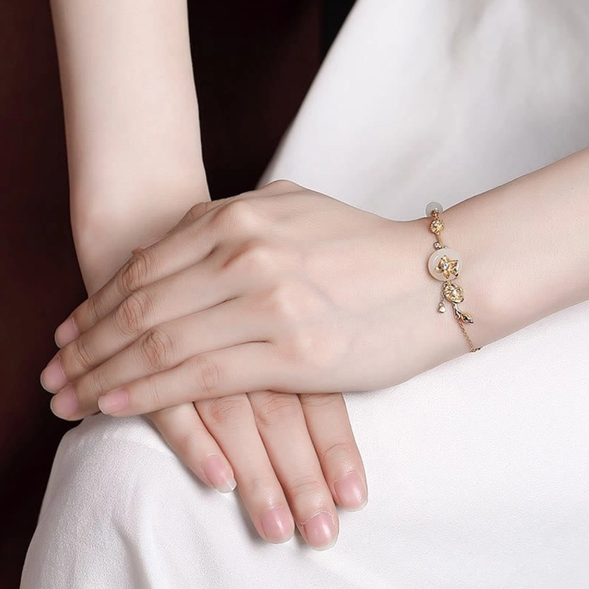 Slim Hetian jade lotus charm bracelet worn on female wrist in lifestyle photo with gold-toned metal accents