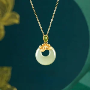 Hetian jade lotus peace buckle necklace with gold-plated silver chain, flatlay with gold leaf decoration