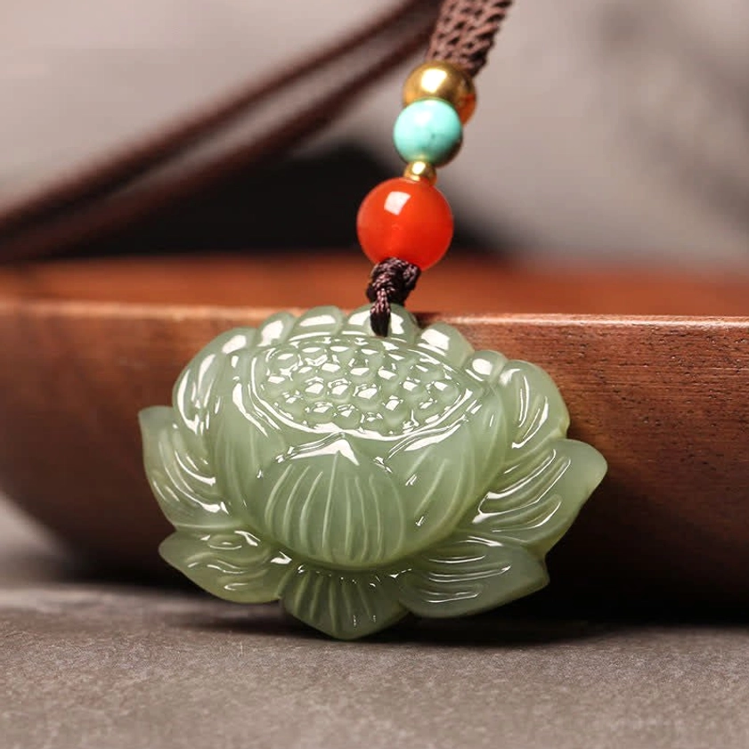Buddhist jade lotus pendant close-up three-quarter view on wooden tray, displaying intricate carved petal texture and detail of pale green jade stone