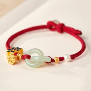 Hetian jade peace buckle lotus bracelet with red braided cord, enamel lotus charm, and pearl accent on neutral tabletop