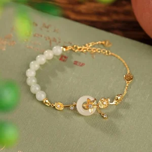Gold-plated sterling silver Hetian jade peace buckle lotus bracelet with adjustable chain, displayed on vintage calligraphy paper