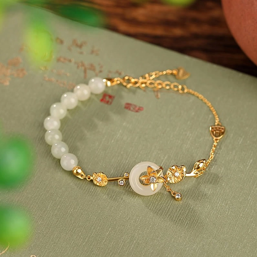 Gold-plated sterling silver Hetian jade peace buckle lotus bracelet with adjustable chain, displayed on vintage calligraphy paper