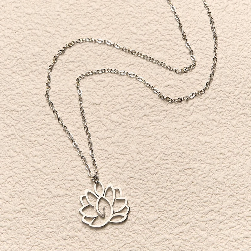 Lotus pendant necklace in top-down flat lay on textured beige wall, silver cable chain with hollow lotus charm detail