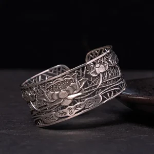 Silver plated hollow lotus open cuff bracelet with intricate relief carving, displayed on dark ceramic plate, showing antique silver finish and adjustable design