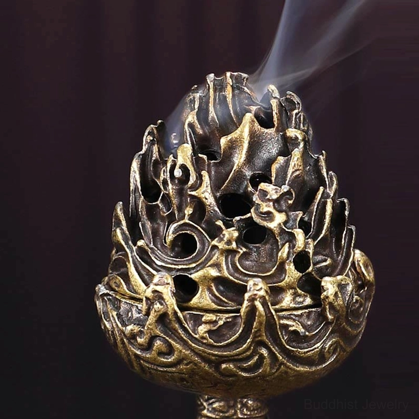 Hollowed Buddhist incense burner close-up front view featuring detailed mountain carvings with rising smoke, dark maroon backdrop