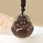 Ice obsidian laughing Buddha pendant close-up with polished dark brown finish and woven accent cord on light background