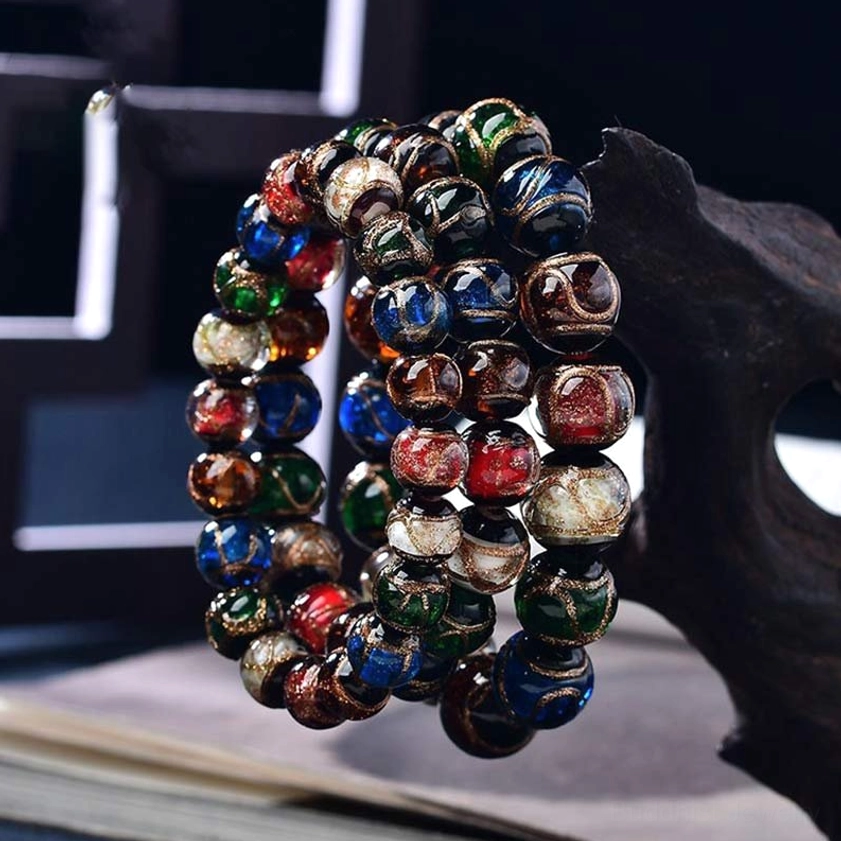 Stacked Buddhist glass bead bracelets in jewel tones displayed with wooden ornament and book