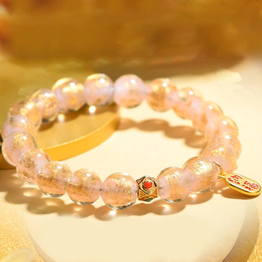 Pink-gold glitter liuli glass beads with gold Fu character charm and decorative metal spacer beads on white display base