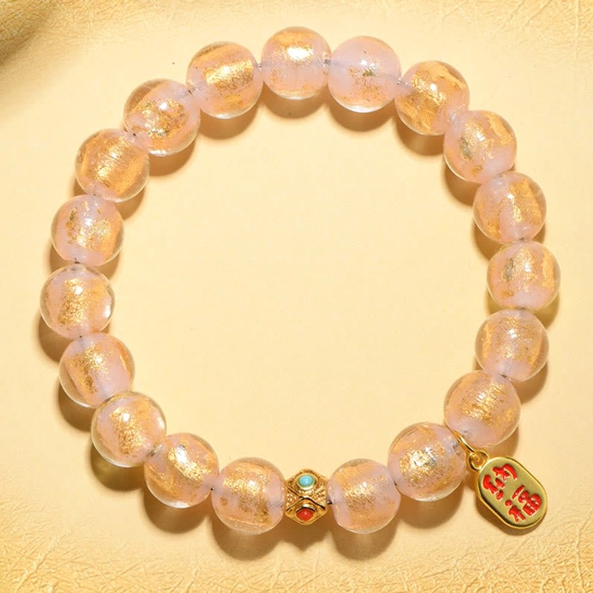 Translucent pink gold-sand filled liuli glass beads with gold Fu fortune charm and metal spacers on beige background