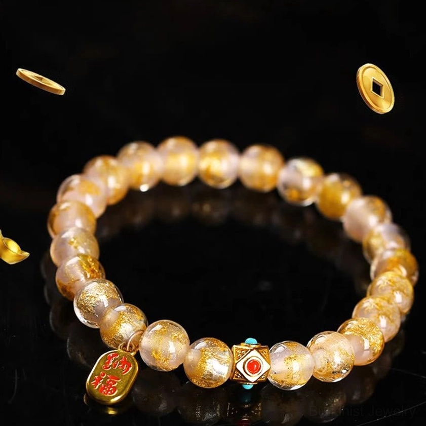 Pink gold-sand liuli glass beads with red enamel metal spacer and Zhao Cai gold charm on dark black background with floating metal elements