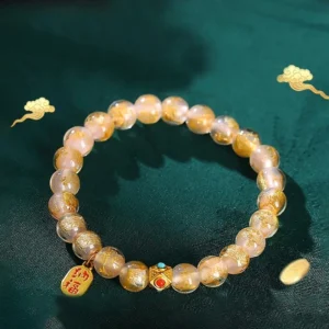 Pale pink incense ash liuli glass beads with gold Fu character charm and enamel spacers on dark green background