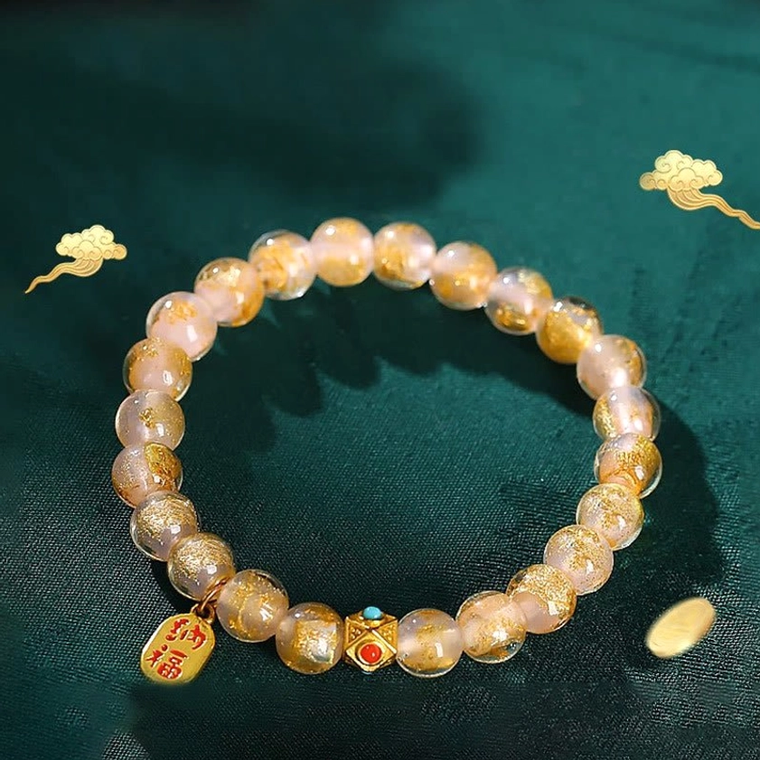 Pale pink incense ash liuli glass beads with gold Fu character charm and enamel spacers on dark green background