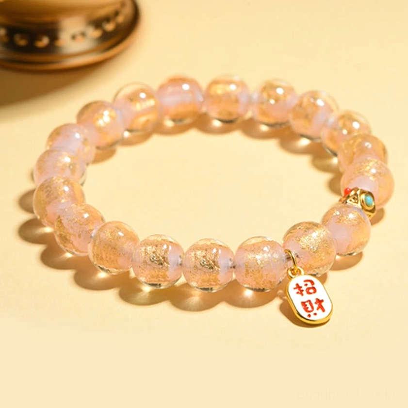Pink glitter glass beads with round Zhao Cai wealth charm and enamel accents on wooden surface