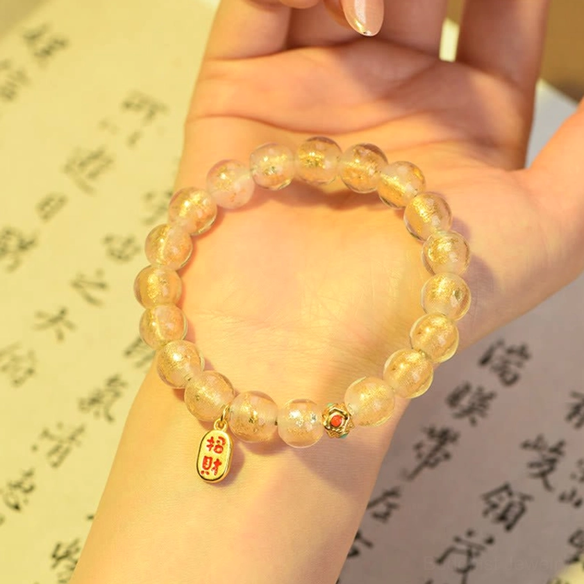 Side view of incense ash liuli glass bracelet on wrist with gold tone beads glitter glass accents and Fu fortune charm vintage calligraphy backdrop