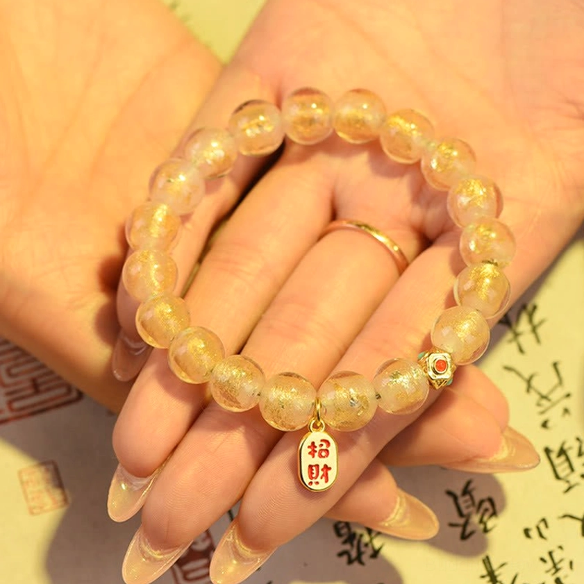 Hand-wearing incense ash liuli glass bracelet with matte gold beads and glitter glass accents Zhao Cai pendant on calligraphy background