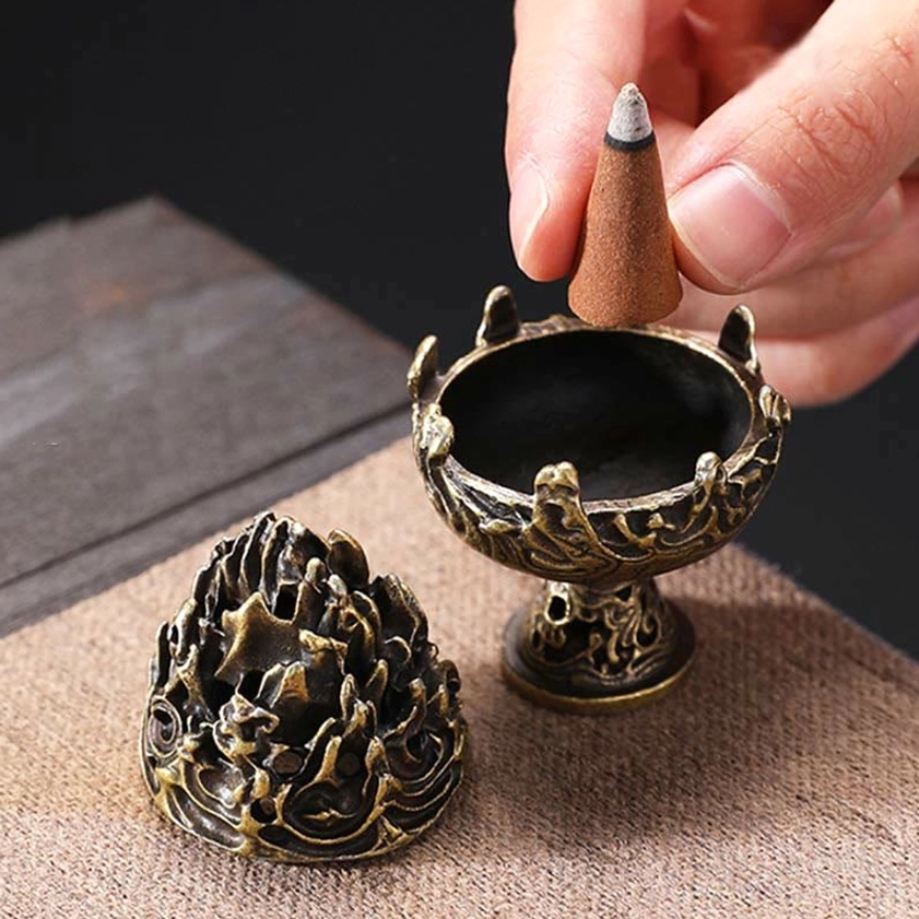 Detachable incense burner top-down view showing two separable parts with hand placing cone incense, linen cloth background
