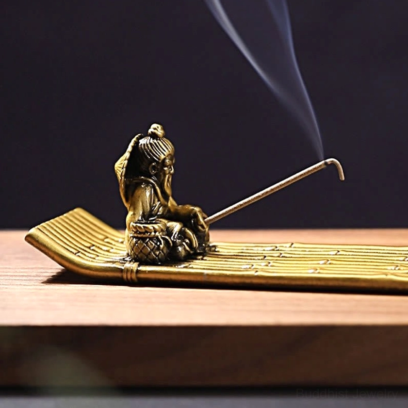 Close-up detail of handmade fisherman sculpture on incense burner with curved incense stick and smoking aromatics