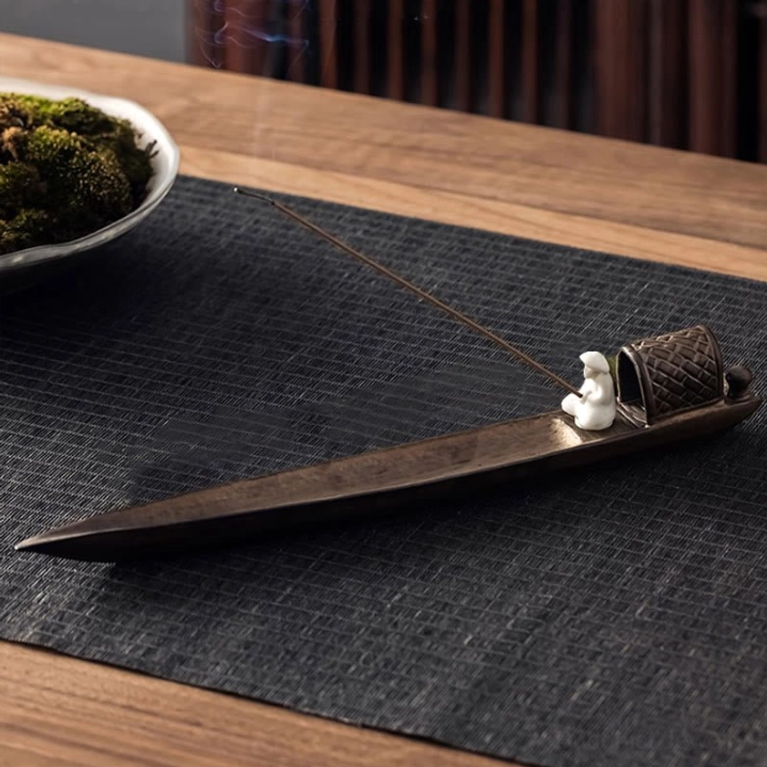 Eye-level view of Buddhist ceramic incense holder with seated fisherman figurine and faint incense aroma