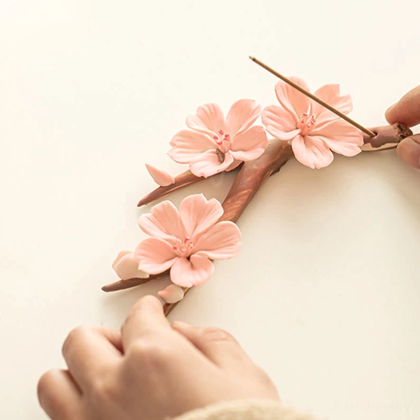 Hands adjusting incense stick on plum blossom ceramic holder, side overhead view showing product interaction