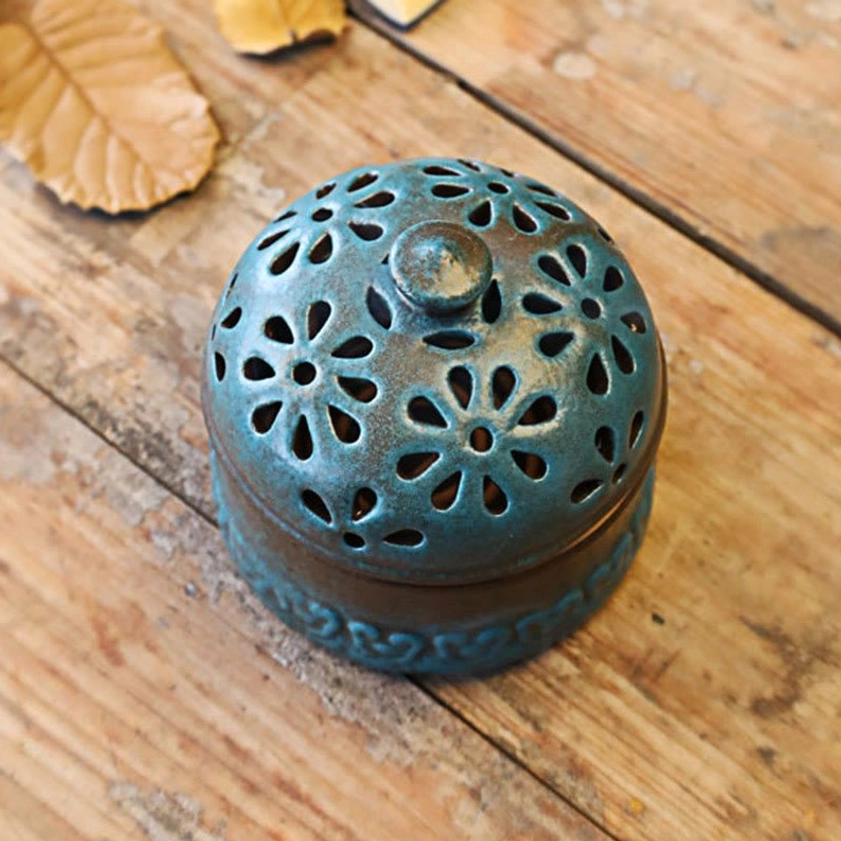 Overhead close-up view of ceramic incense burner lid featuring detailed floral hollow carvings with round ceramic finial knob on teal finish