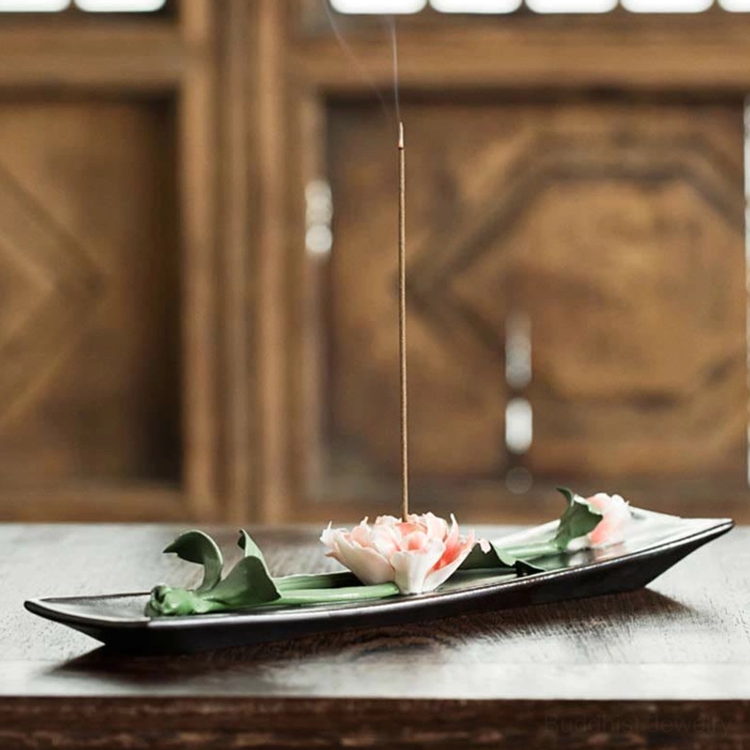 Lotus themed ceramic incense burner with lit incense stick burning, traditional wooden interior setting
