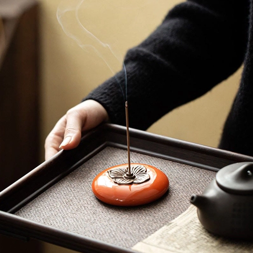 Persimmon incense burner placed on wooden tray with black teapot, burning incense with curling smoke in traditional tea ceremony scene