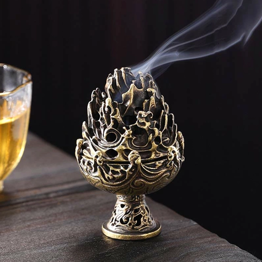 Bronze Buddhist incense burner displayed on wooden tea table with glass of beverage, showing vintage finish and ornate relief details