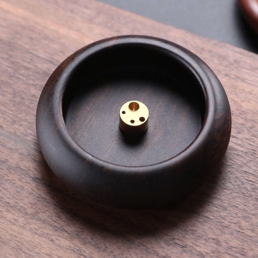 Top-down view of round wood incense tray with brass multi-hole insert on wooden surface