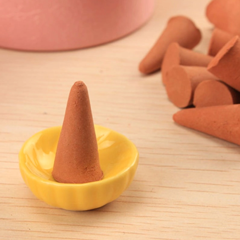 Single incense cone burning on lotus-shaped yellow ceramic holder, side eye-level view