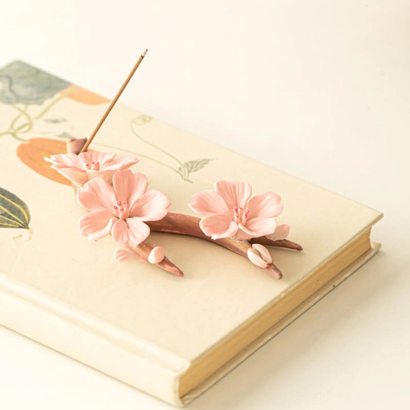 Plum blossom ceramic incense burner displayed on hardcover book with painted plant motifs, meditation room decoration