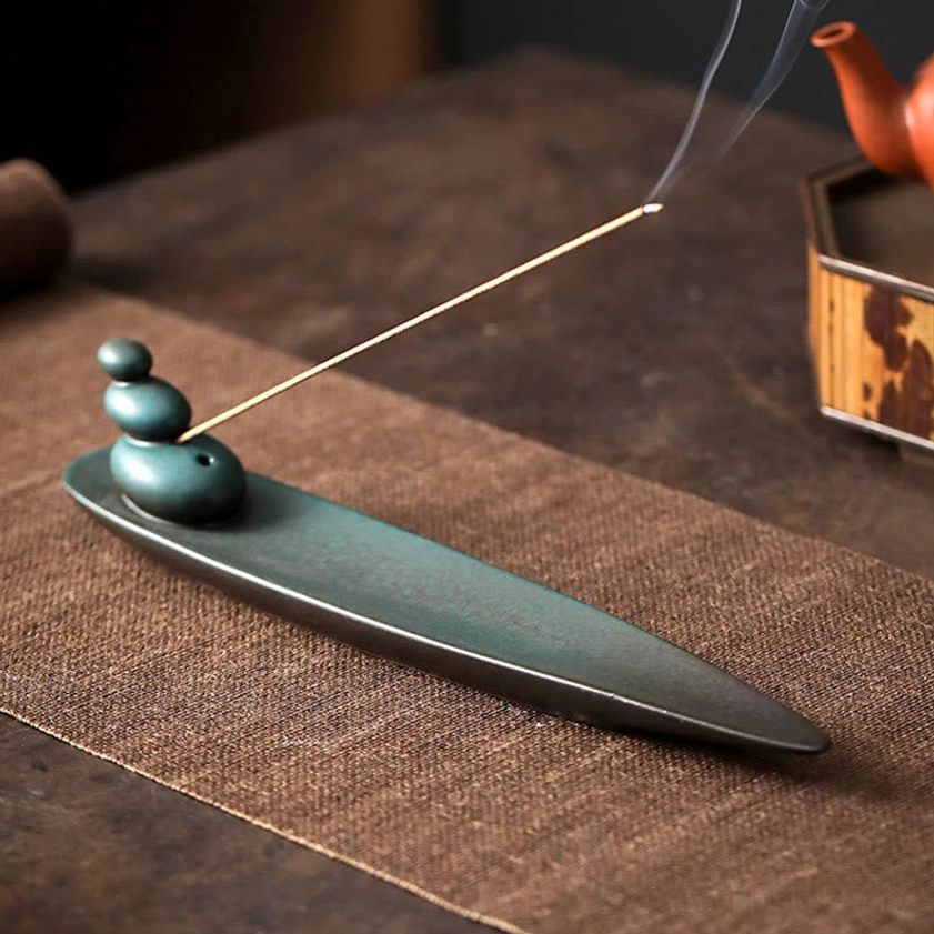 Ceramic incense holder with lit incense displaying stacked stone design on tea table with traditional tea ware