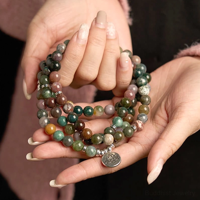 Multi-strand 108 Indian agate mala bracelet with lotus pendant held in hand against pink fabric