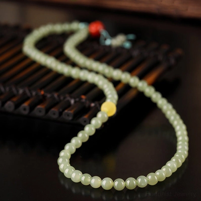 Long jade prayer necklace mala with 108 beads, amber accent, red laughing Buddha charm, light blue tassel on bamboo tray