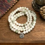 108 jade mala beads bracelet with silver lotus pendant on wooden surface, flat lay view showing white and green jade beads